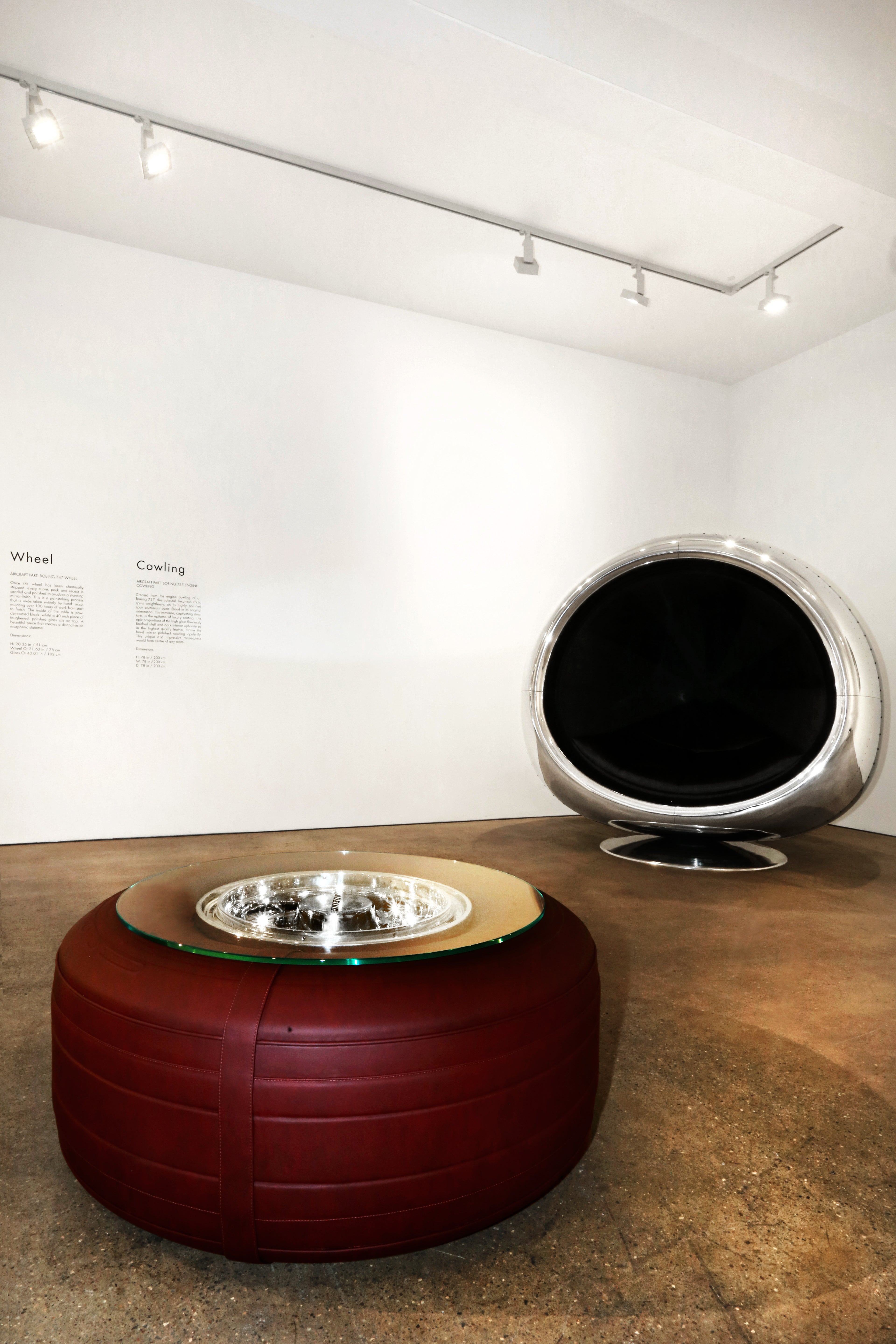 A Boeing 747 wheel coffee table with tire wrapped in red leather at gallery with chair. 